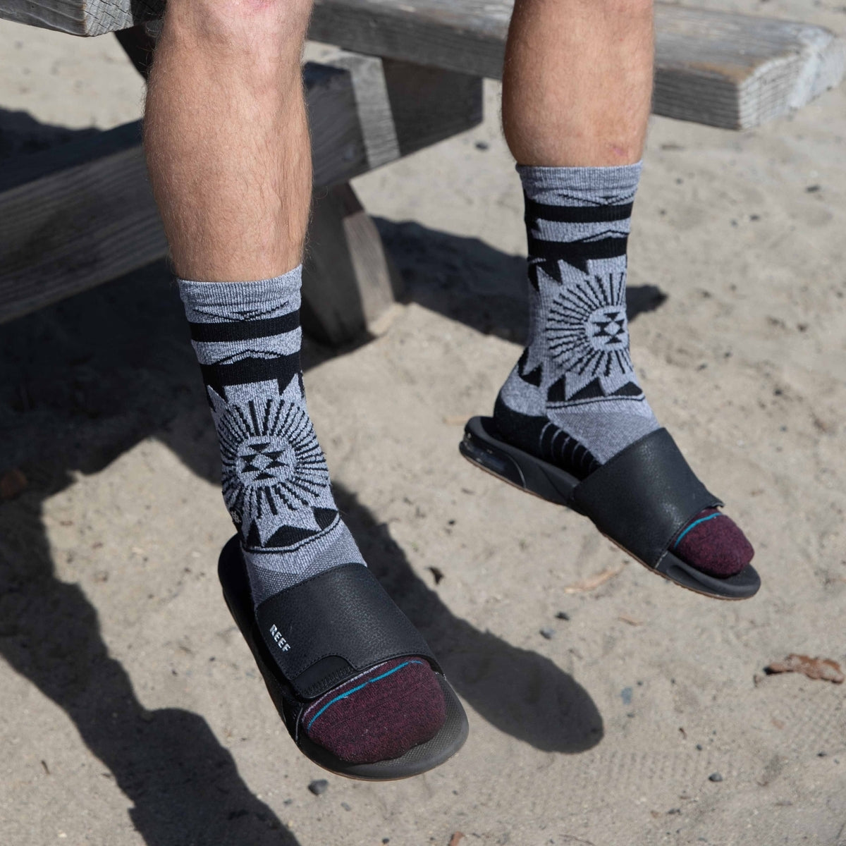 Fanning Slide footwear facing forward on feet with patterned socks, showing cushioned, water-friendly black slides.